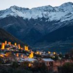 View of the Svanetian towers with night illumination in Mestia village against snowy mountains at sunrise. Upper Svaneti, Georgia.