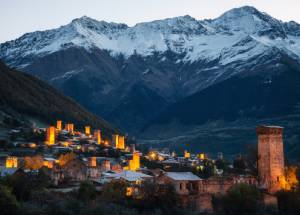 View of the Svanetian towers with night illumination in Mestia village against snowy mountains at sunrise. Upper Svaneti, Georgia.