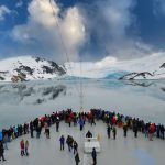 People aboard a cruise ship near snow covered mountain in Antartica.