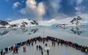 People aboard a cruise ship near snow covered mountain in Antartica.