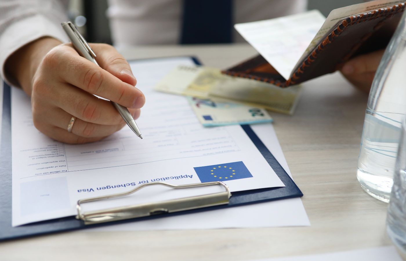 A man holding a passport and writing with a pen on a form