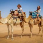 Women sitting on a camel in desert.