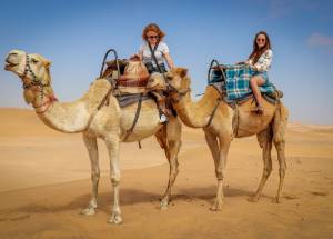 Women sitting on a camel in desert.