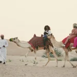 Women riding camels on desert.