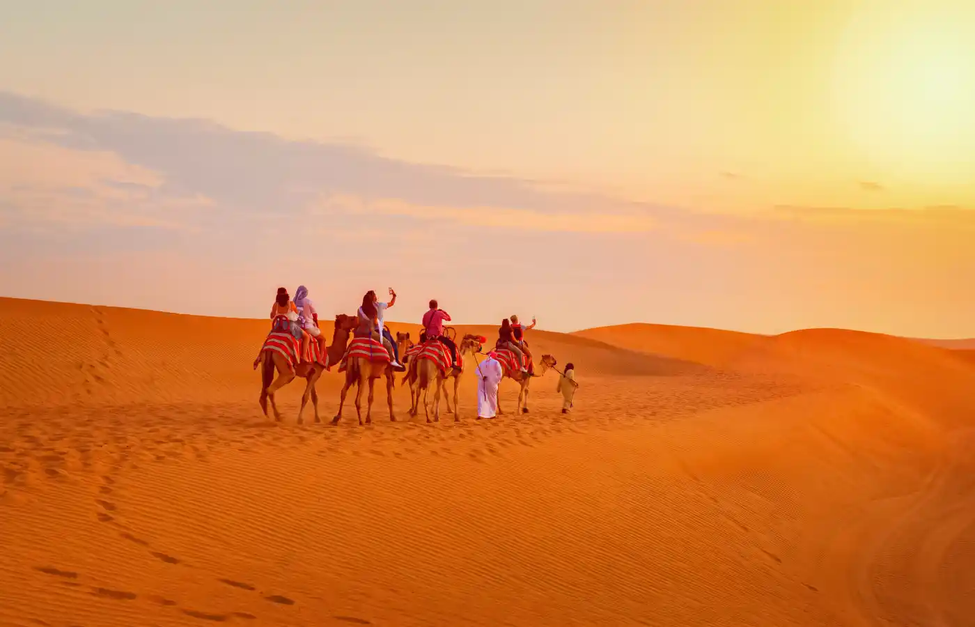 Caravan with group of tourists riding camels through Dubai desert