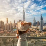 Woman with a white hat is standing on a balcony in front of the skyline from Dubai Downtown