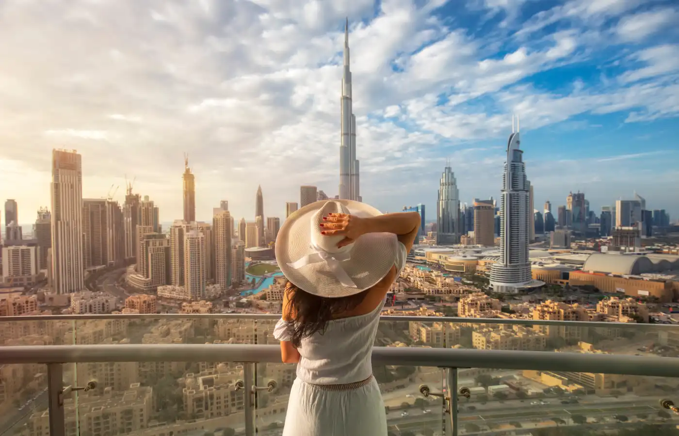 Woman with a white hat is standing on a balcony in front of the skyline from Dubai Downtown