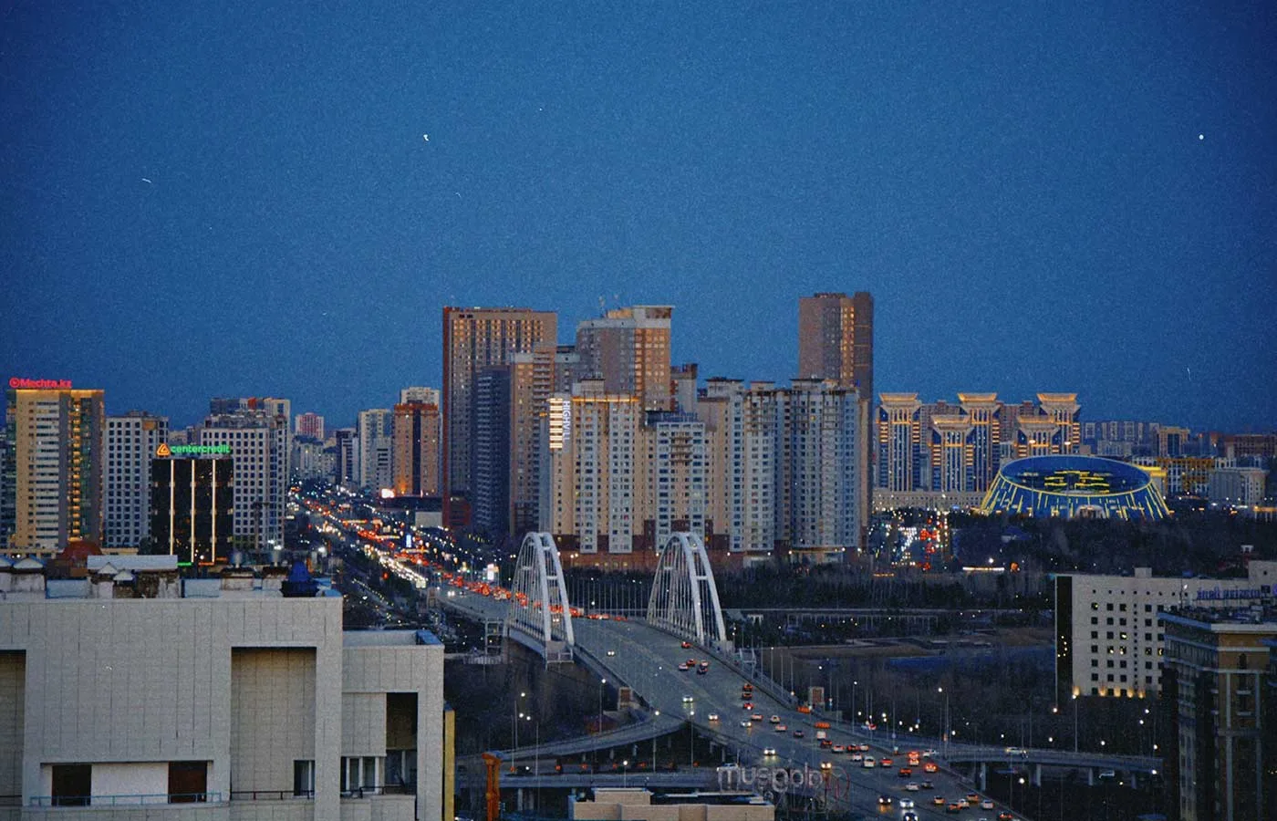 Almaty skyline at night with illuminated bridge.