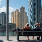an elderly couple seated on a bench observing the Dubai creek overlooking buildings of Dubai